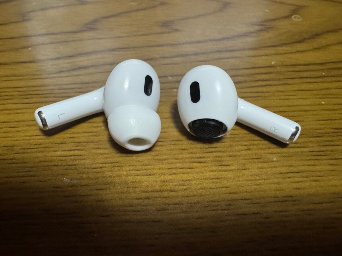 木目のテーブルに置かれたAirPods Pro（第2世代）の左右のイヤホンで、片側のみイヤーチップを外した状態