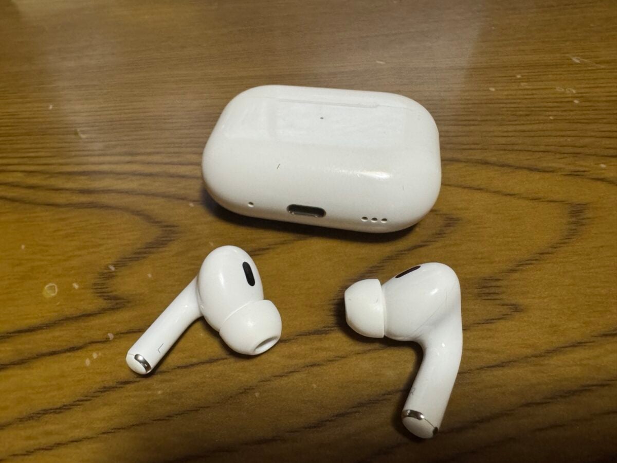 木目のテーブルに置かれたAirPods Pro（第2世代）と充電ケース、イヤーチップを装着した左右のイヤホン
